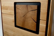 Nahaufnahme aus schräger Frontperspektive: Massivholz-Möbelfront aus Eiche mit quadratischer Einlage eines Hirnholz-Blocks, sichtbar mit Jahresringen und Rissen, eingerahmt von dunklem Rahmen.