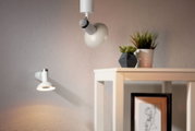Zwei LED-Leuchten an der Wand und Decke, moderne Einrichtung mit Pflanzen und Kunstwerk im Hintergrund, seitliche Perspektive