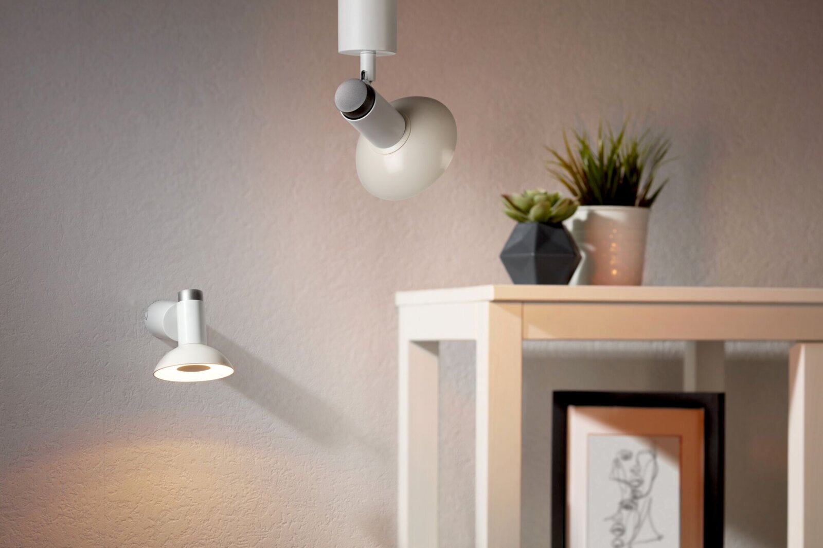Zwei LED-Leuchten an der Wand und Decke, moderne Einrichtung mit Pflanzen und Kunstwerk im Hintergrund, seitliche Perspektive