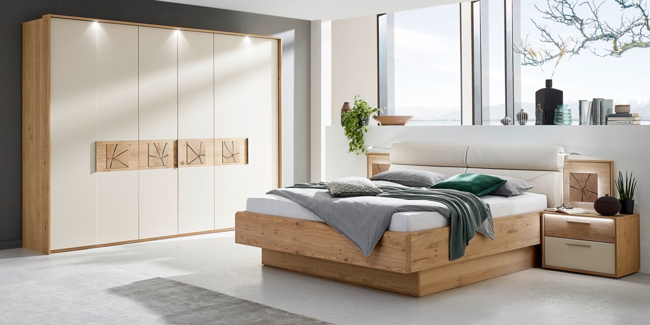 Moderner, sechstüriger Drehtürenschrank in Holzoptik mit cremefarbenen Türen, dekorativen Holzpaneelen und integrierter Beleuchtung, aus der Perspektive eines stilvoll eingerichteten Schlafzimmers.