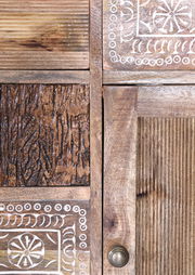 Nahaufnahme eines Möbelstücks mit verschiedenen Holzstrukturen und dekorativen Schnitzereien, Perspektive von vorne.