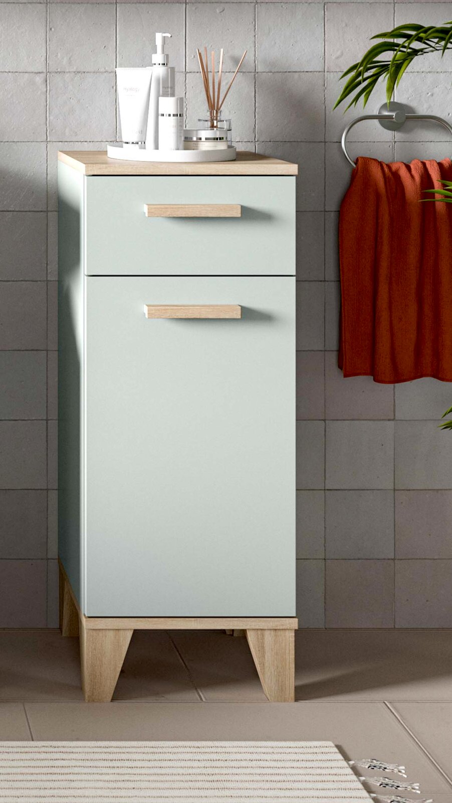 MID.YOU Badschrank halbhoch STAR Schmaler Bad-Unterschrank in Mintgrün mit Holzplatte, Holzgriffen und hohen Holzfüßen, mit zwei Schubladen, frontal leicht von links fotografiert vor grauer Fliesenwand