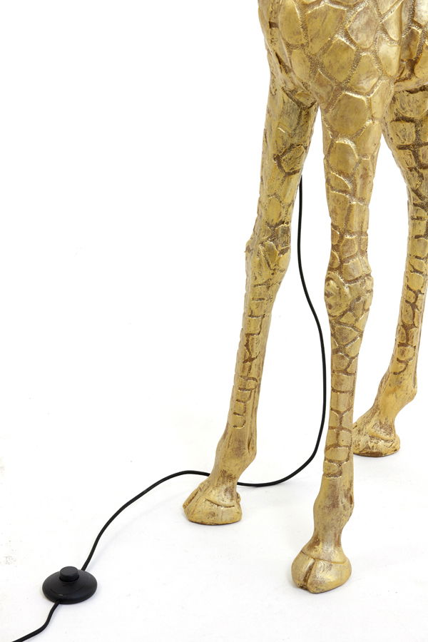 Nahaufnahme der Beine einer goldenen Stehleuchte in Form einer Giraffe, mit einem schwarzen Kabel und Fußschalter auf weißem Hintergrund.