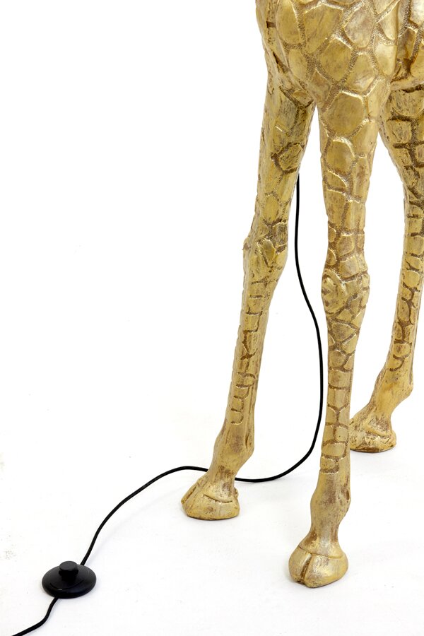 Close-up van de poten van een gouden staande lamp in de vorm van een giraffe, met een zwarte kabel en een voetschakelaar op een witte achtergrond.