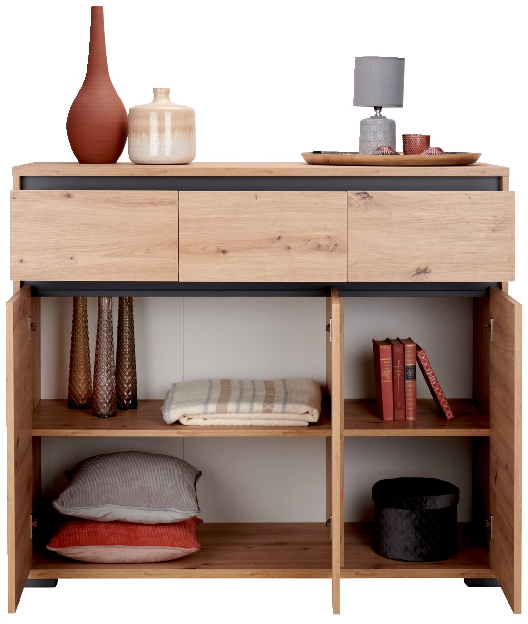 Houten dressoir met drie lades en open deuren, gevuld met decoratieartikelen en textiel, gezien vanuit de voorkant.