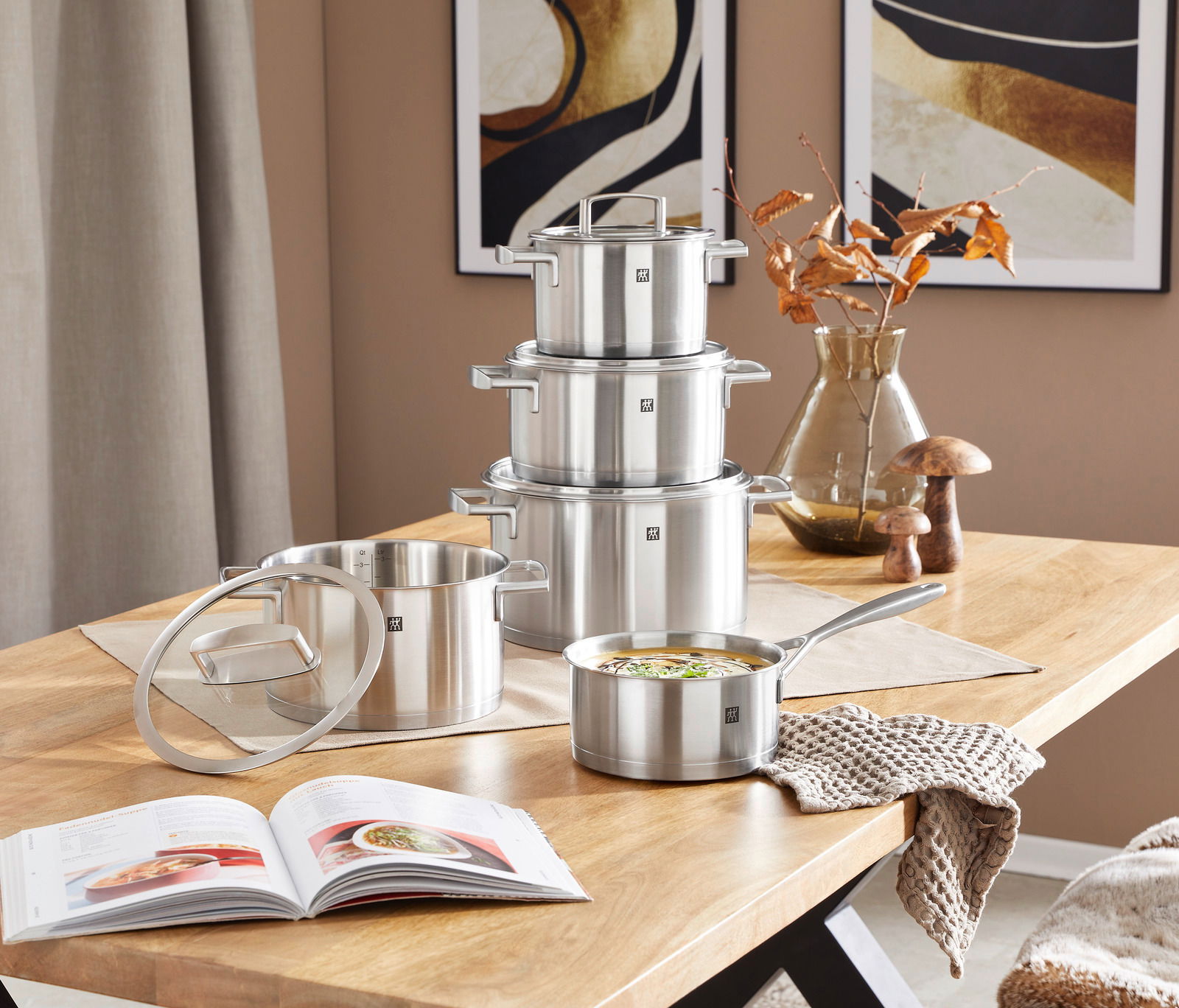 Topfset Vitality 5-tlg. aus Edelstahl auf einem Holztisch, bestehend aus vier Töpfen und einer Stielkasserolle, mit einem modernen, minimalistischen Design. Perspektive von vorne.