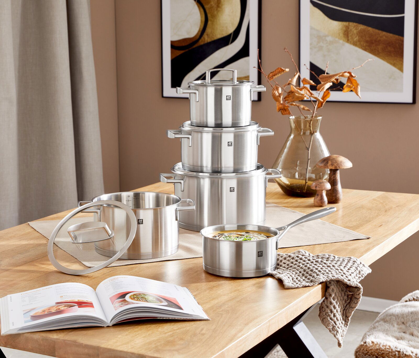 Topfset Vitality 5-tlg. aus Edelstahl auf einem Holztisch, bestehend aus vier Töpfen und einer Stielkasserolle, mit einem modernen, minimalistischen Design. Perspektive von vorne.