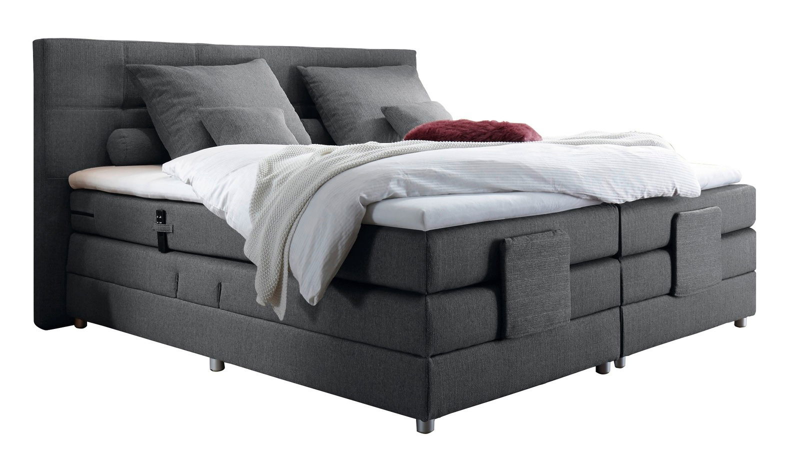 Graues Boxspringbett mit Kopfteil, seitliche Perspektive, dekoriert mit Kissen und Decken.