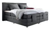 Graues Boxspringbett mit Kopfteil, seitliche Perspektive, dekoriert mit Kissen und Decken.