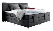 Graues Boxspringbett mit Kopfteil, seitliche Perspektive, dekoriert mit Kissen und Decken.