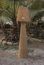 Akku-Outdoor-Stehleuchte aus Rattan in einem Garten mit Palmen, seitliche Perspektive