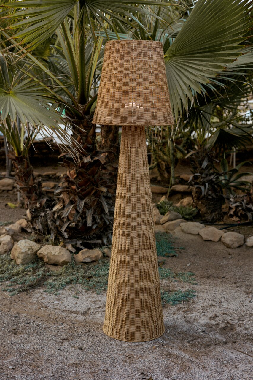 Akku-Outdoor-Stehleuchte aus Rattan in einem Garten mit Palmen, seitliche Perspektive