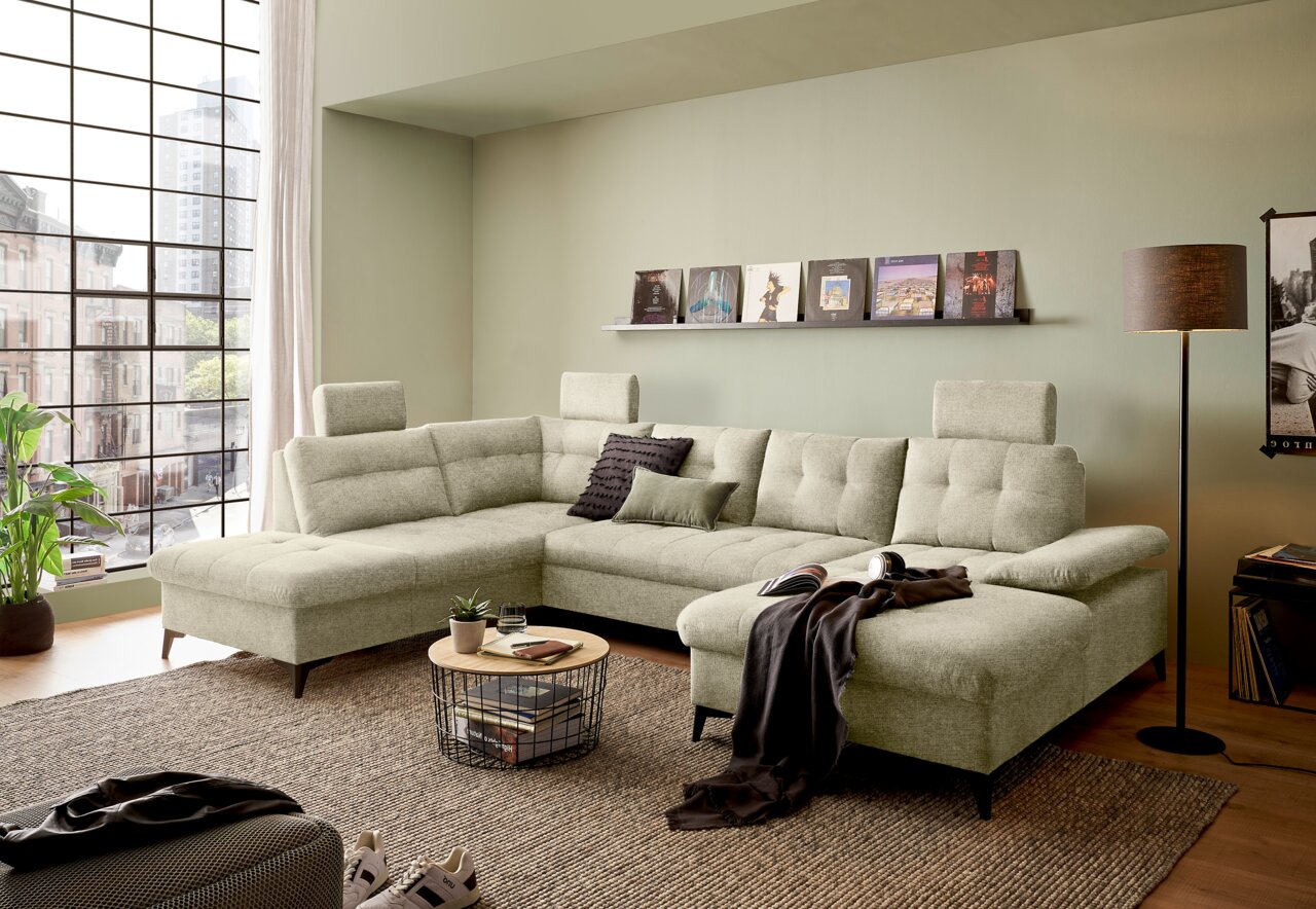 Großes, modernes U-förmiges Sofa in einem hellen Wohnzimmer mit großen Fenstern, aus der Perspektive von vorne links betrachtet.