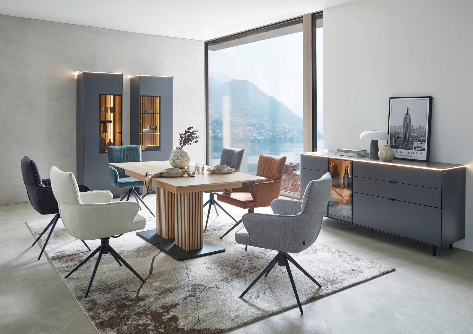 Moderner Essbereich mit einem großen Holztisch und verschiedenen gepolsterten Stühlen in einem hellen Raum mit Blick auf einen See.