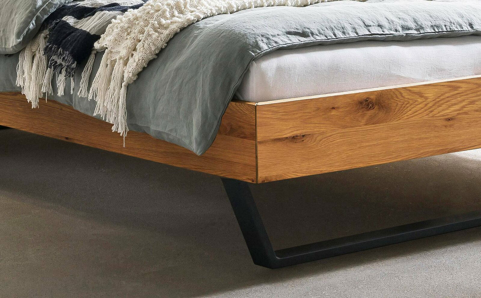 Nahaufnahme eines modernen Bettgestells aus Holz mit schwarzem Metallfuß, seitliche Perspektive