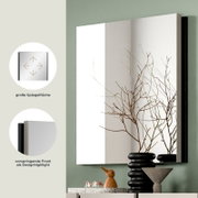 Moderner Wandspiegel mit großer Spiegelfläche und vorspringender Front als Designhighlight, in schräger Frontansicht an grüner Wand über Sideboard dekoriert