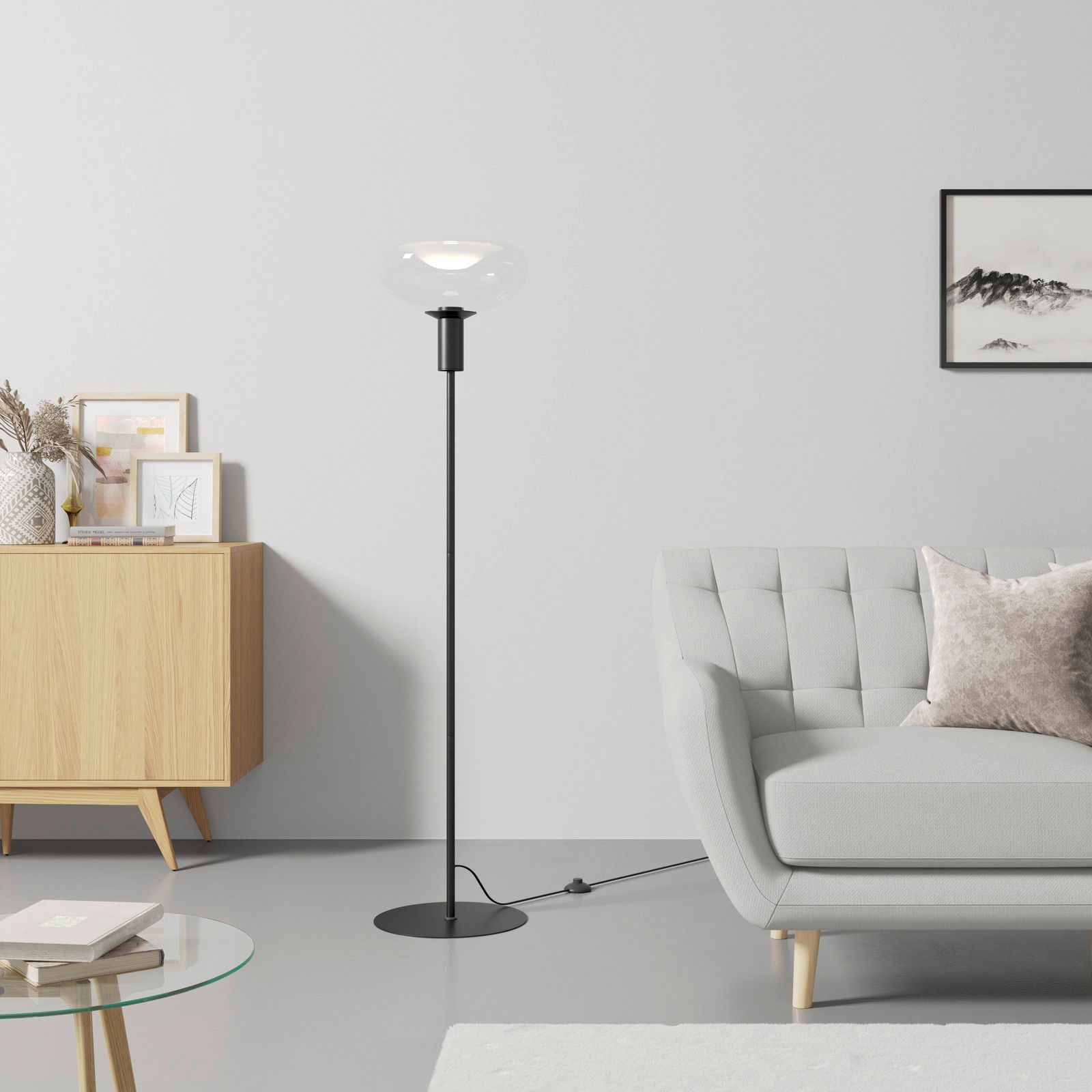 Dieter Knoll Stehleuchte Moderne Stehleuchte mit schwarzem Ständer und klarem Glasschirm, seitliche Perspektive im Wohnzimmer mit Sofa und Sideboard.