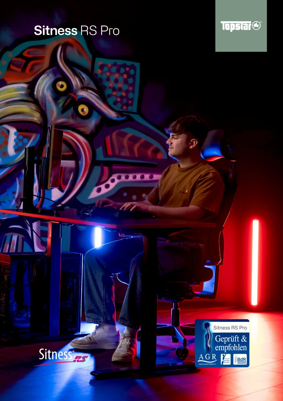 Zijaanzicht van een jonge man die aan een bureau zit in een Sitness RS Pro-gamingstoel, omringd door kleurrijke verlichting en graffitikunst.