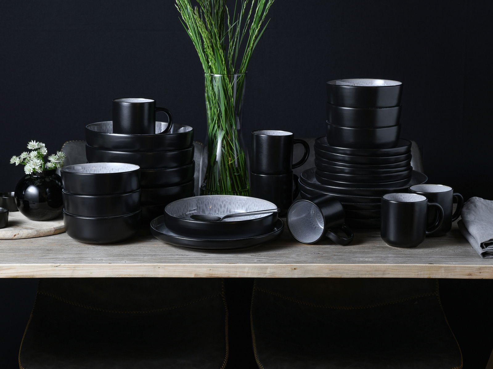 Schwarzes Kombiservice 30-tlg. Frost auf einem Tisch, bestehend aus Tellern, Schalen und Tassen, in einer eleganten, modernen Anordnung von vorne betrachtet.