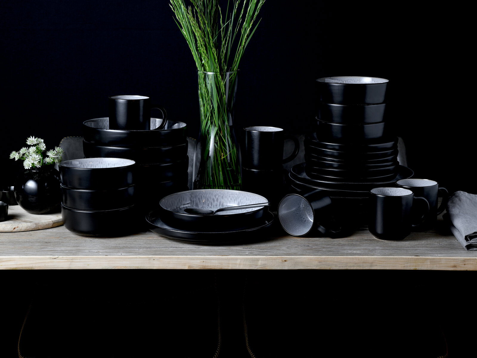 Schwarzes Kombiservice 30-tlg. Frost auf einem Tisch, bestehend aus Tellern, Schalen und Tassen, in einer eleganten, modernen Anordnung von vorne betrachtet.