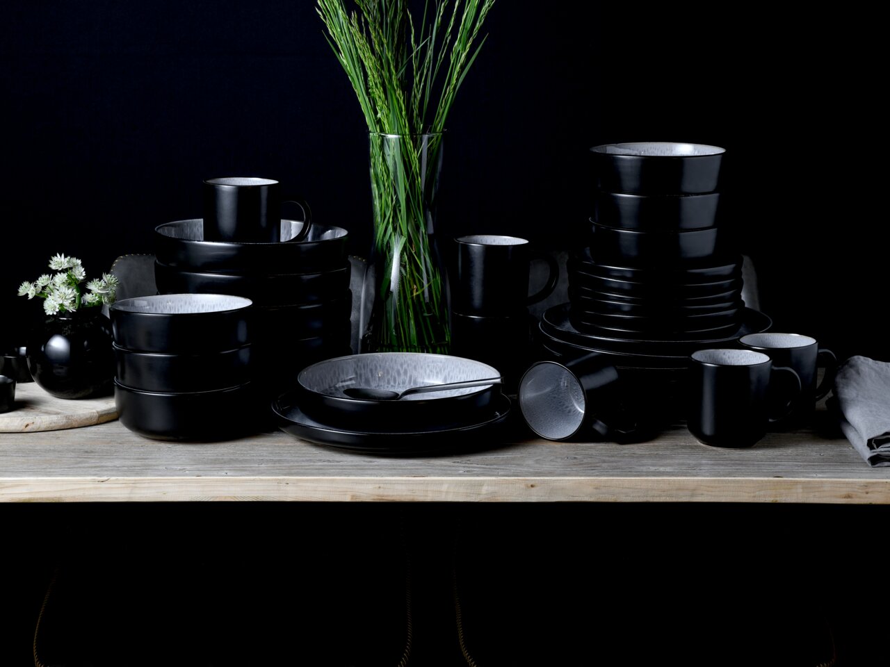 Schwarzes Kombiservice 30-tlg. Frost auf einem Tisch, bestehend aus Tellern, Schalen und Tassen, in einer eleganten, modernen Anordnung von vorne betrachtet.