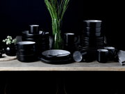 Schwarzes Kombiservice 30-tlg. Frost auf einem Tisch, bestehend aus Tellern, Schalen und Tassen, in einer eleganten, modernen Anordnung von vorne betrachtet.