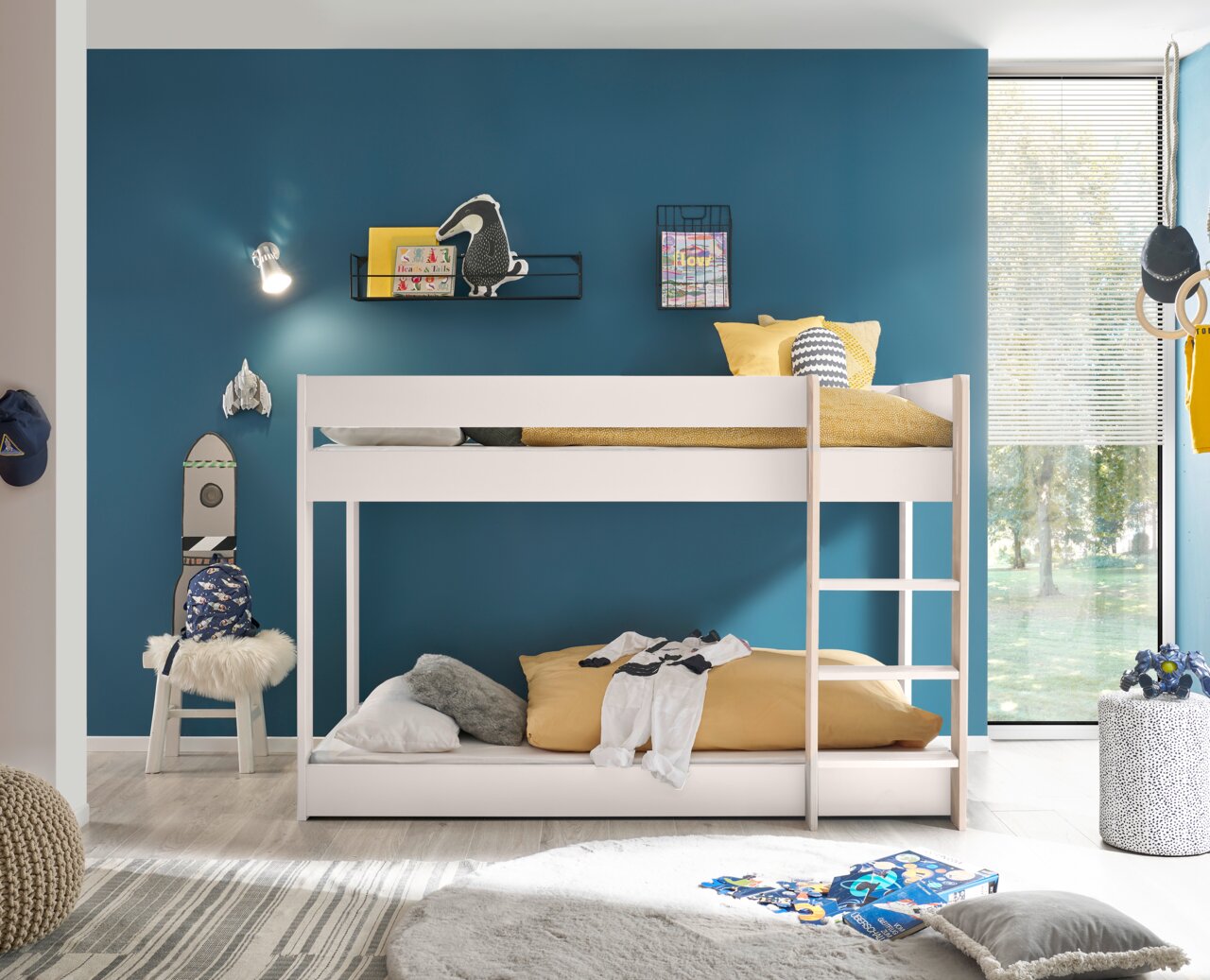 Modernes weißes Etagenbett in einem stilvoll eingerichteten Kinderzimmer mit blauer Wand und großen Fenstern, seitliche Perspektive.
