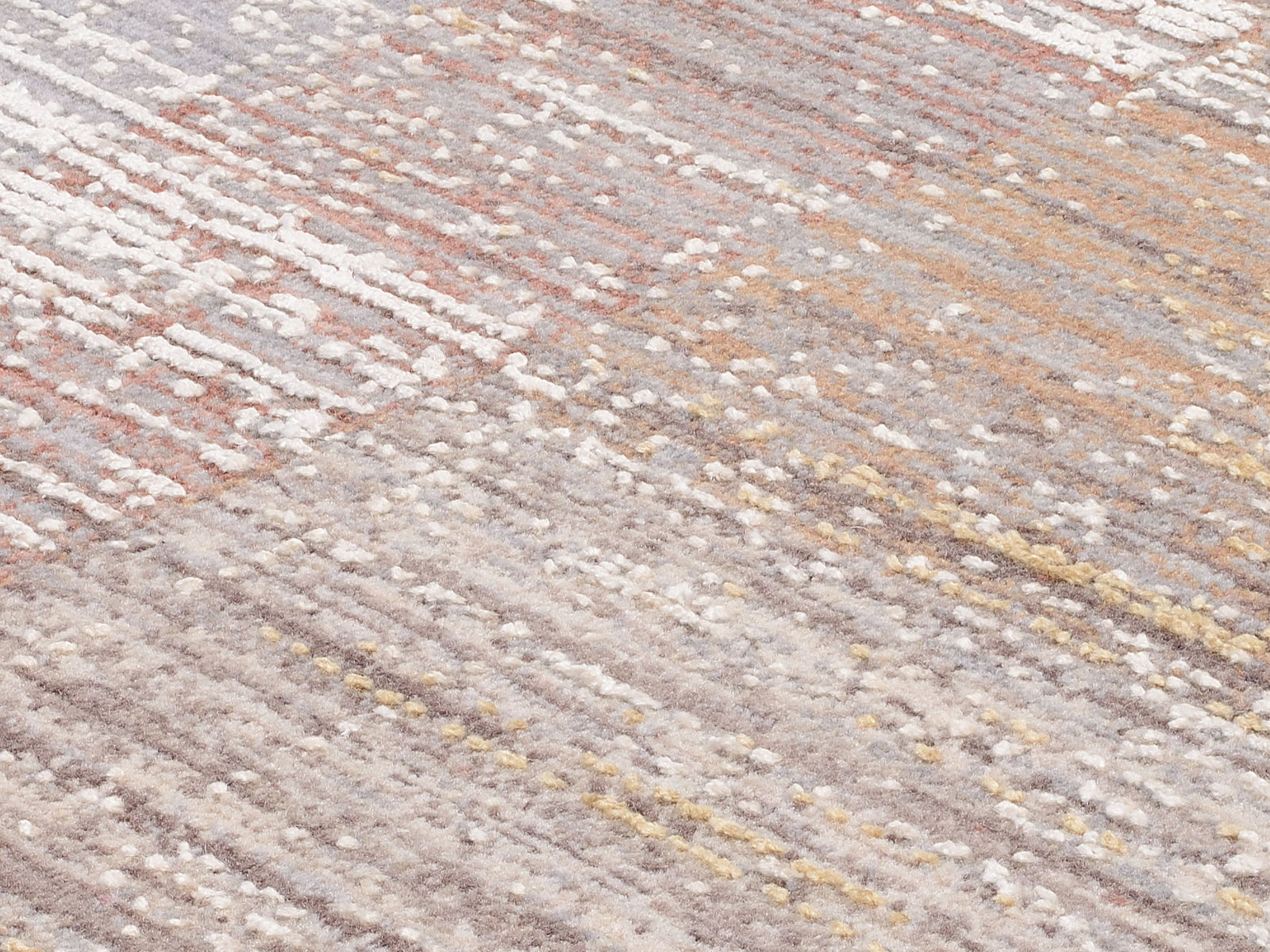 Nahaufnahme eines Designer-Teppichs mit einem modernen, mehrfarbigen Muster in Erdtönen und Pastellfarben, schräg von oben fotografiert.