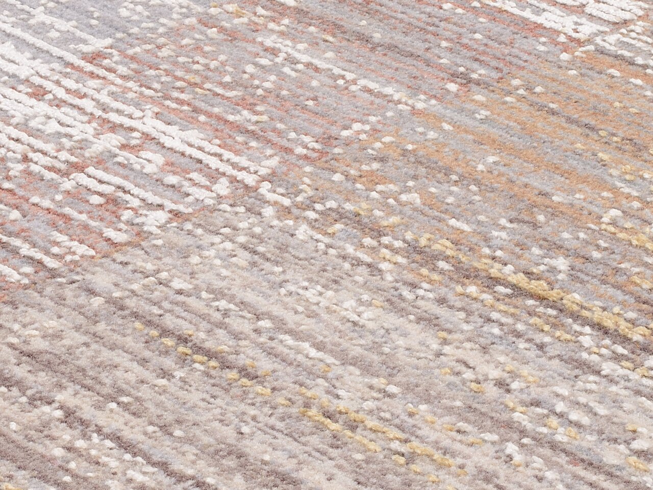 Nahaufnahme eines Designer-Teppichs mit einem modernen, mehrfarbigen Muster in Erdtönen und Pastellfarben, schräg von oben fotografiert.