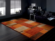 Frisé-Teppich in warmen Rot- und Orangetönen mit geometrischem Muster, in einem modernen Wohnzimmer mit dunklem Holzboden und grauem Sofa, aus der Perspektive von schräg oben fotografiert.