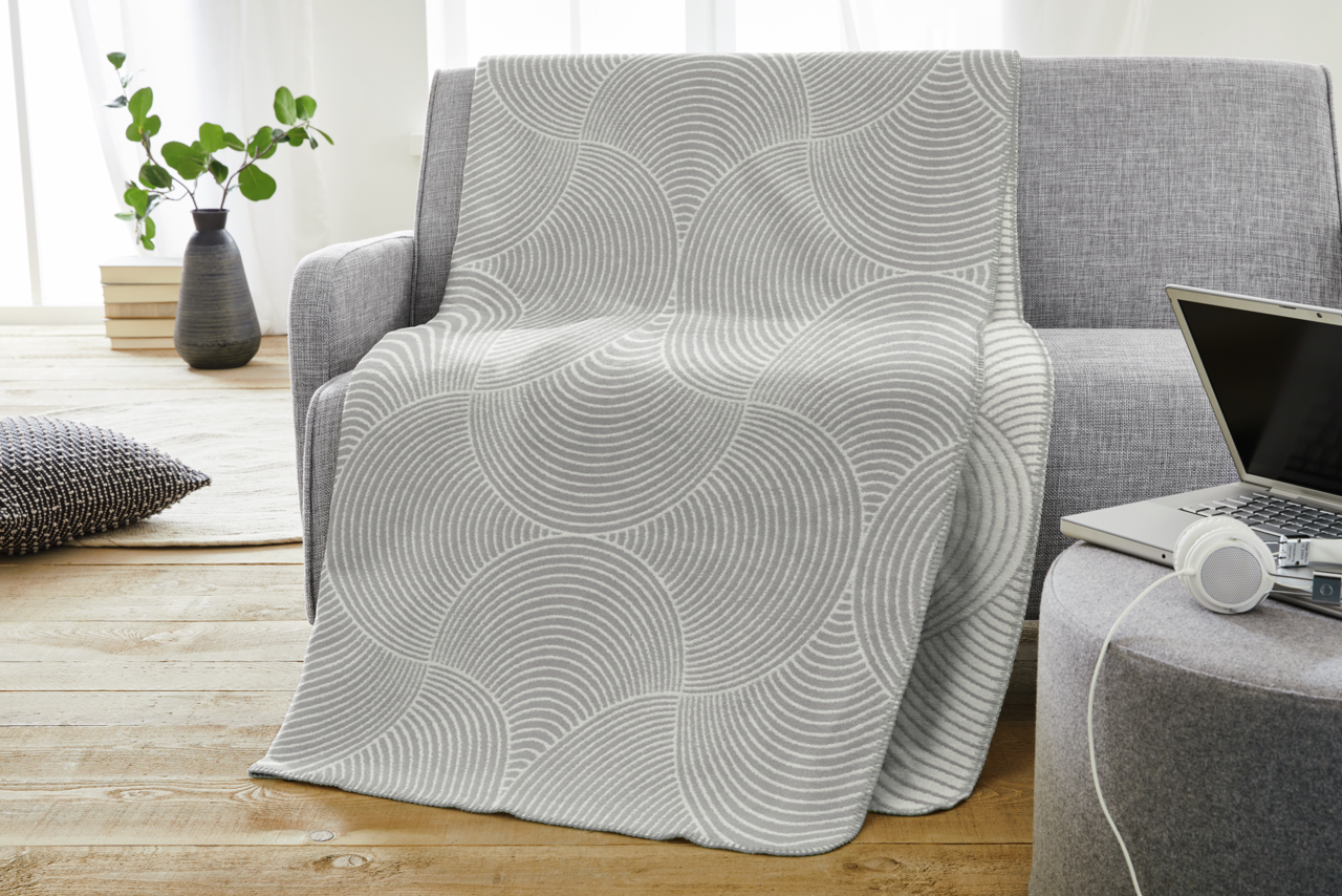 Graue Jacquard Decke mit kreisförmigem Muster auf einem Sofa drapiert, seitliche Perspektive.