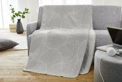 Graue Jacquard Decke mit kreisförmigem Muster auf einem Sofa drapiert, seitliche Perspektive.