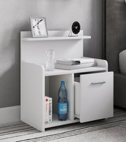 Weißer moderner Nachttisch mit Ablage, offenem Fach und geöffneter Schublade mit Metallgriff, dekoriert mit Bilderrahmen, kleiner Uhr, Büchern und Wasserflasche, fotografiert in leichter Frontansicht von schräg rechts.
