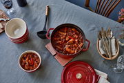 Rote Cocotte 24cm rund von oben mit Eintopf gefüllt, auf einem gedeckten Tisch mit Schalen und Besteck.