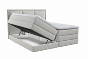 Lichtgrijs gestoffeerd boxspringbed met hoofdbord, topper en geopende opbergruimte, schuin van voren gezien
