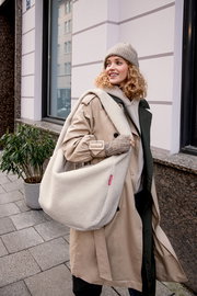 Cremefarbene Teddy-Fleece-Umhängetasche im Oversize-Format mit breitem Schulterriemen, getragen von einer Frau im beigen Trenchcoat in der Stadt; Perspektive: leicht seitliche Ansicht auf Schulterhöhe