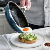 Eine petrolfarbene Stielpfanne, aus der ein Spiegelei auf ein Avocado-Toast serviert wird. Die Pfanne wird aus einer seitlichen Perspektive gezeigt.