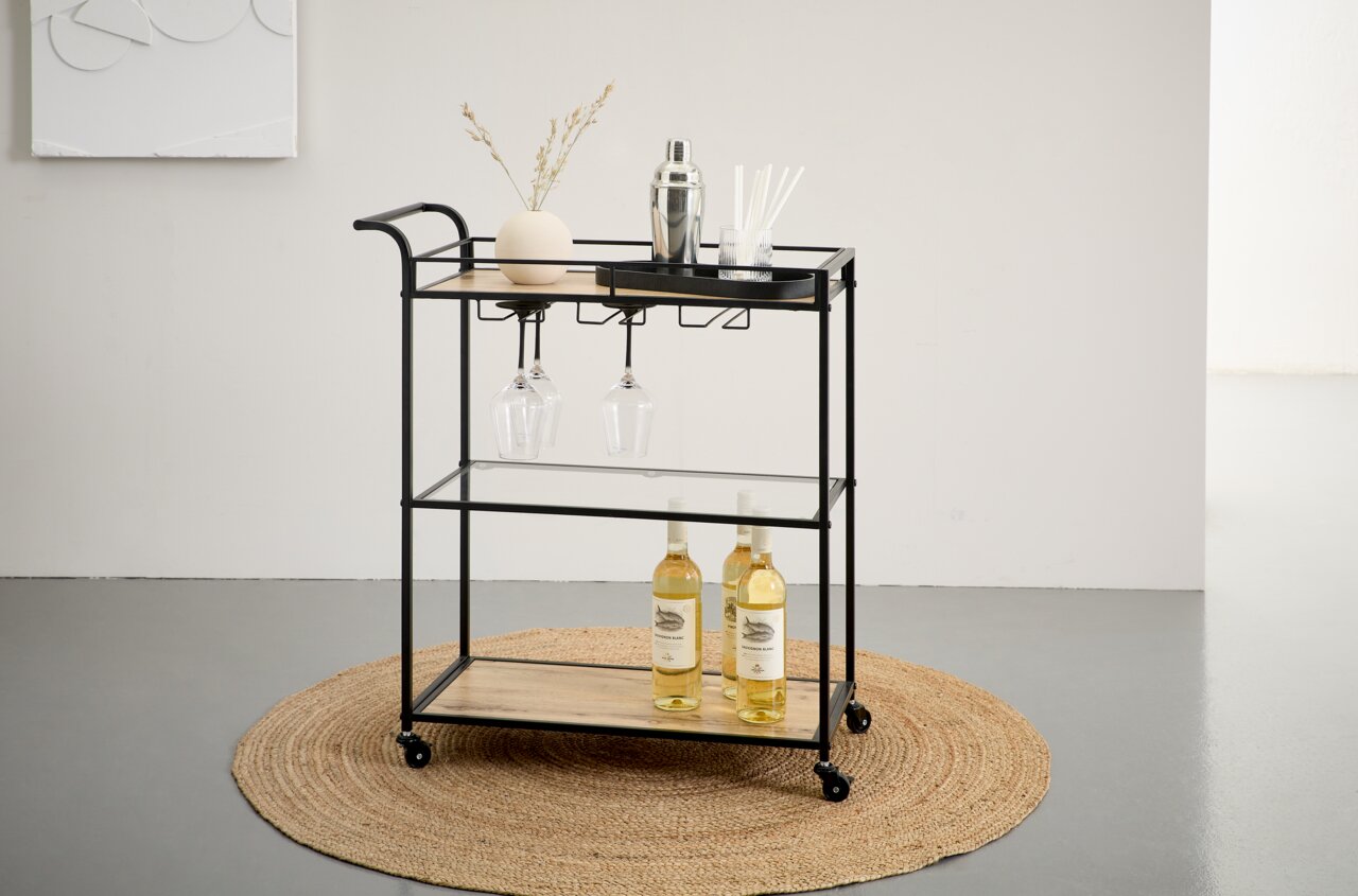 XORA Barwagen MANDY Zwarte barwagen/servierwagen van metaal met houten planken en een glazen bodem, met hangende wijnglazen en flessen, op wieltjes – vooraanzicht in een licht schuin perspectief.