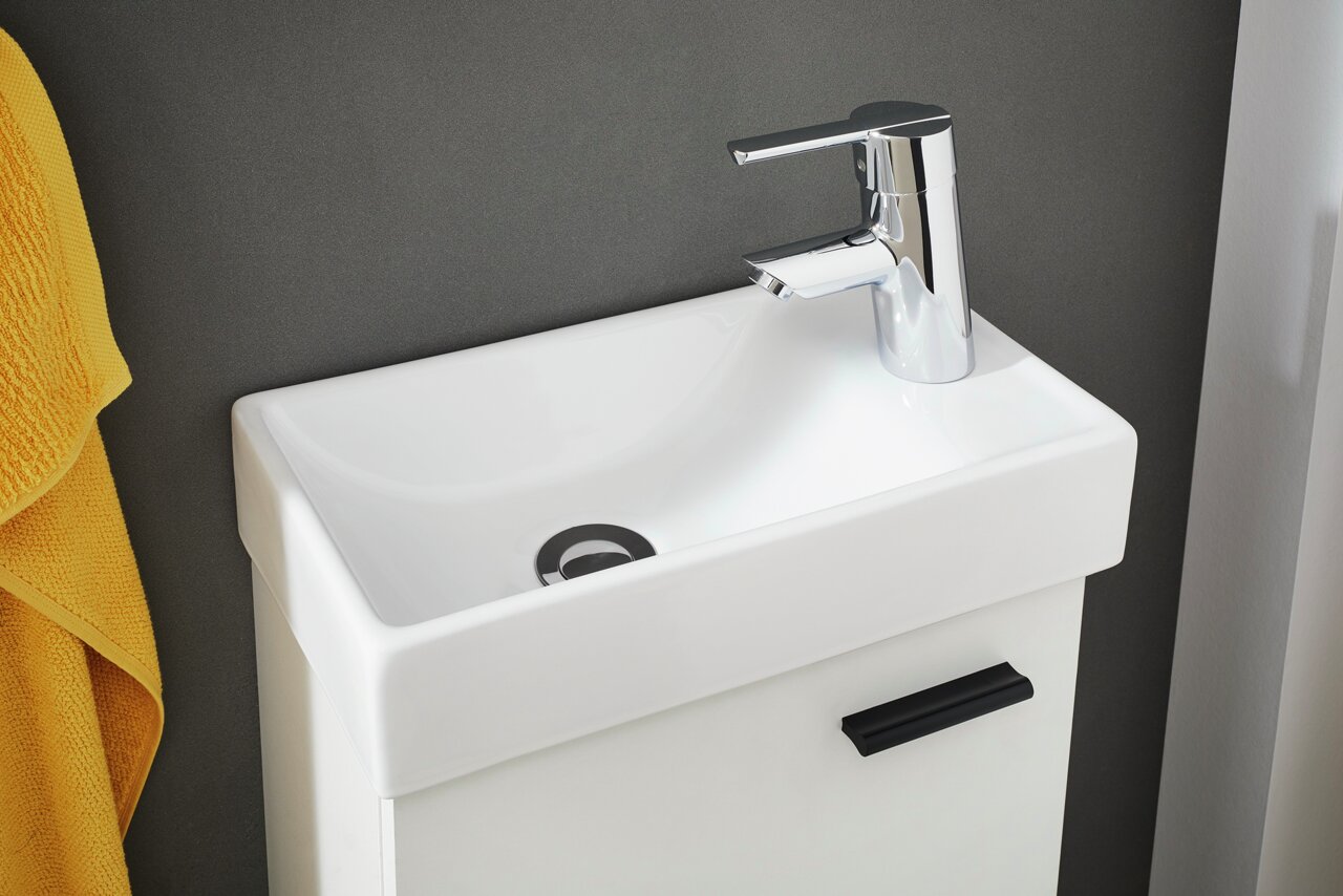 Modernes, rechteckiges Waschbecken mit glänzendem Wasserhahn, seitliche Perspektive, gelbes Handtuch im Hintergrund.