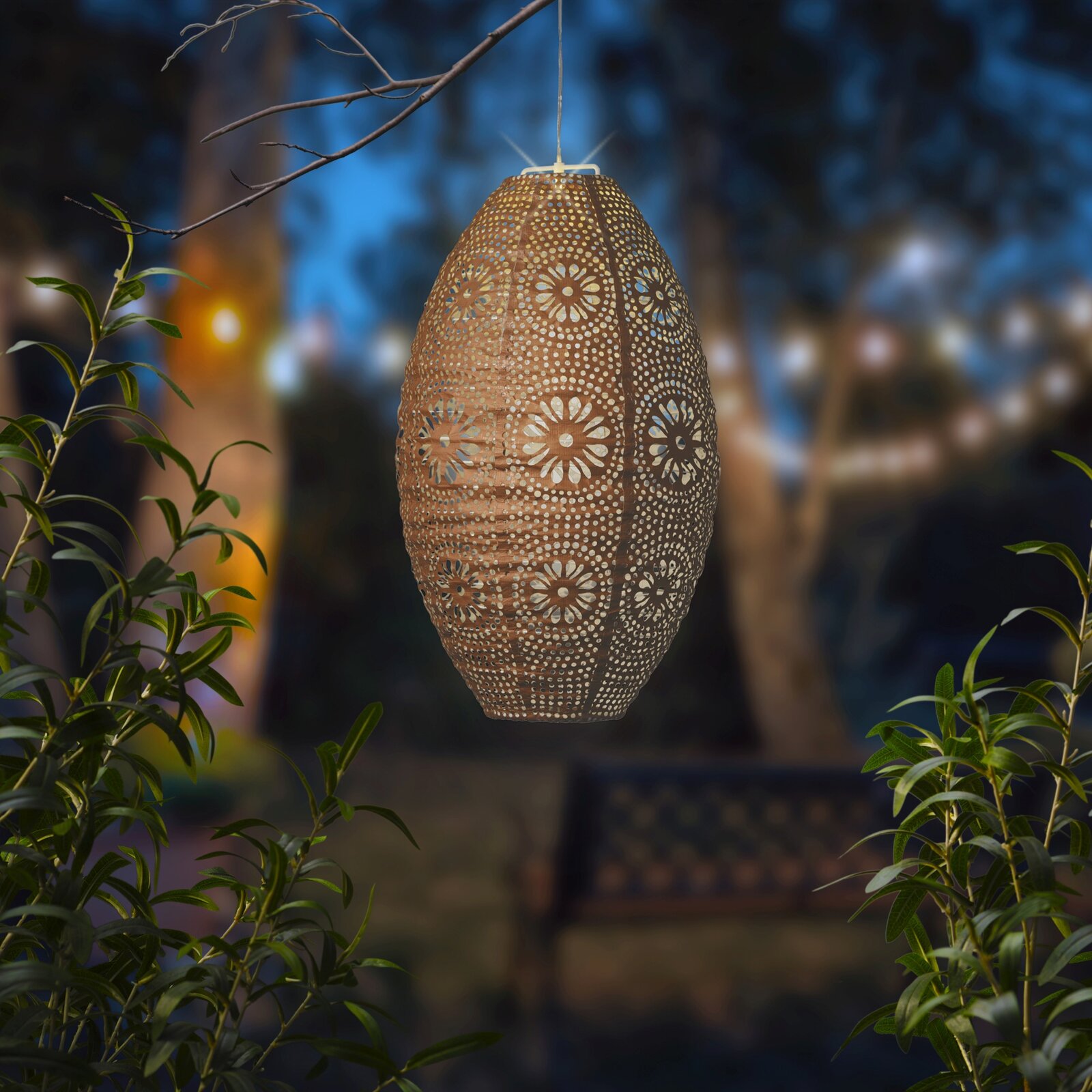 Hangende zonne-lantaarn met filigraan bloemmotief, verlicht in een nachtelijke tuin, zijaanzicht.