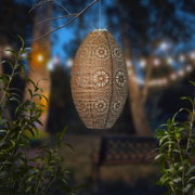 Hangende zonne-lantaarn met filigraan bloemmotief, verlicht in een nachtelijke tuin, zijaanzicht.