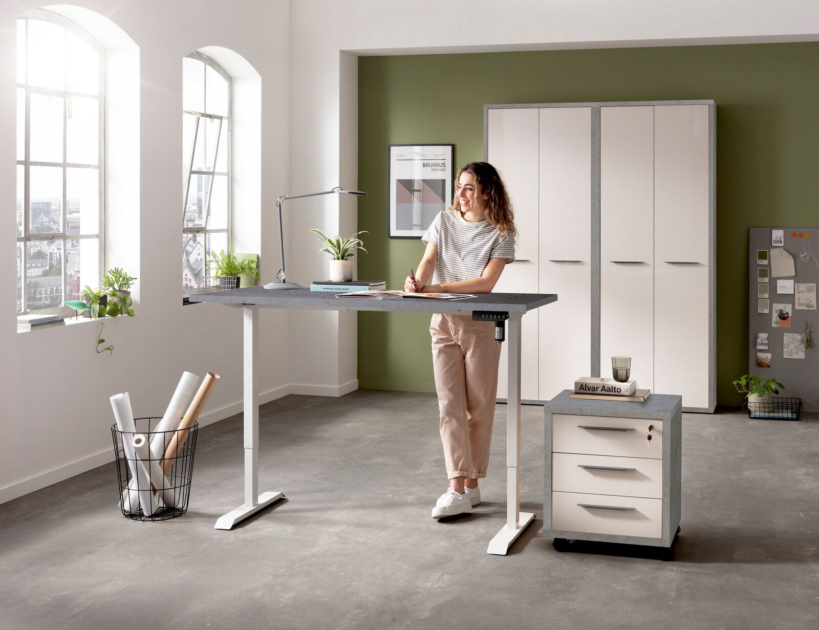 Elektrisches Fußgestell in einem modernen Büro, seitliche Perspektive, mit einer Person, die am höhenverstellbaren Tisch arbeitet.