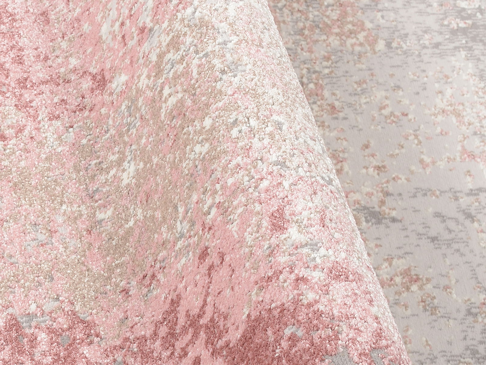 Nahaufnahme eines Designer-Teppichs mit rosa, beige und grauen Farbtönen, aus seitlicher Perspektive aufgenommen.
