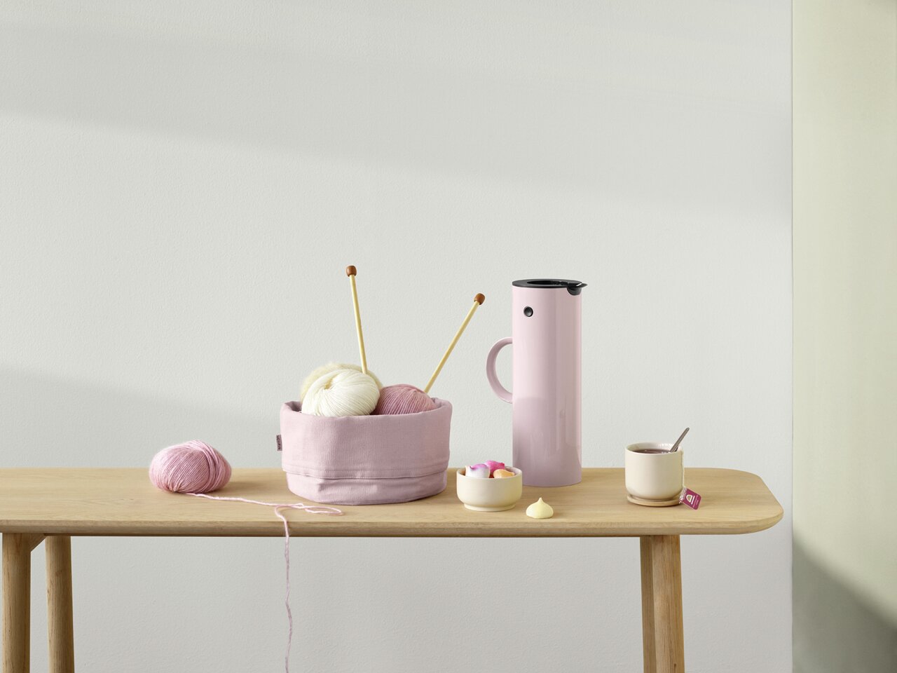 Stelton Isolierkanne Lavendelfarbene Isolierkanne mit Henkel, auf einem Tisch neben Strickzubehör und einer Tasse Tee, seitliche Perspektive.
