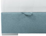 Nahaufnahme eines Boxspringbetts mit hellblauem Stoffbezug und weißer Matratze, seitliche Perspektive