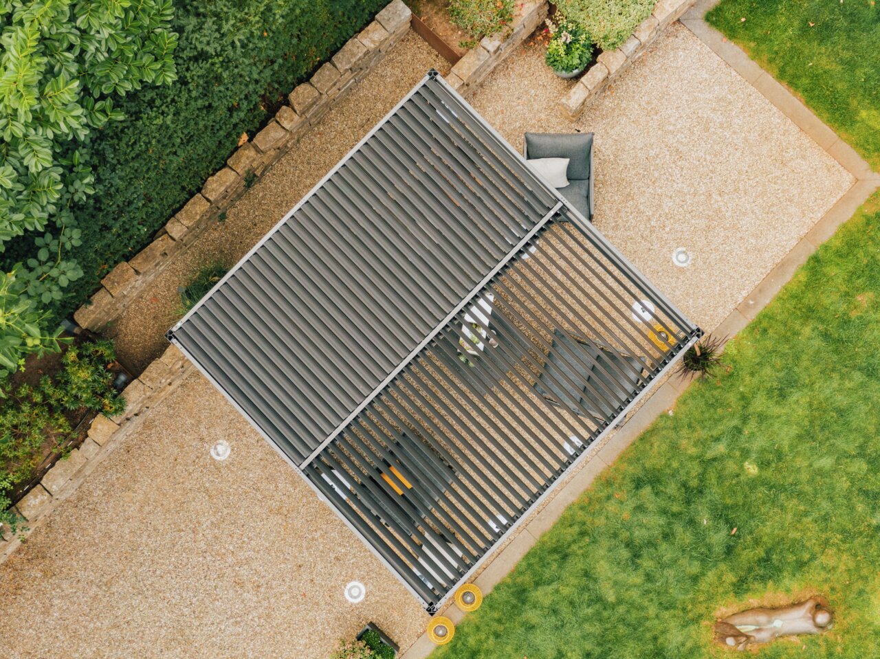 Draufsicht auf eine moderne Terrassenüberdachung mit Lamellen, umgeben von einem gepflegten Garten und Sitzmöbeln.
