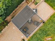 Draufsicht auf eine moderne Terrassenüberdachung mit Lamellen, umgeben von einem gepflegten Garten und Sitzmöbeln.