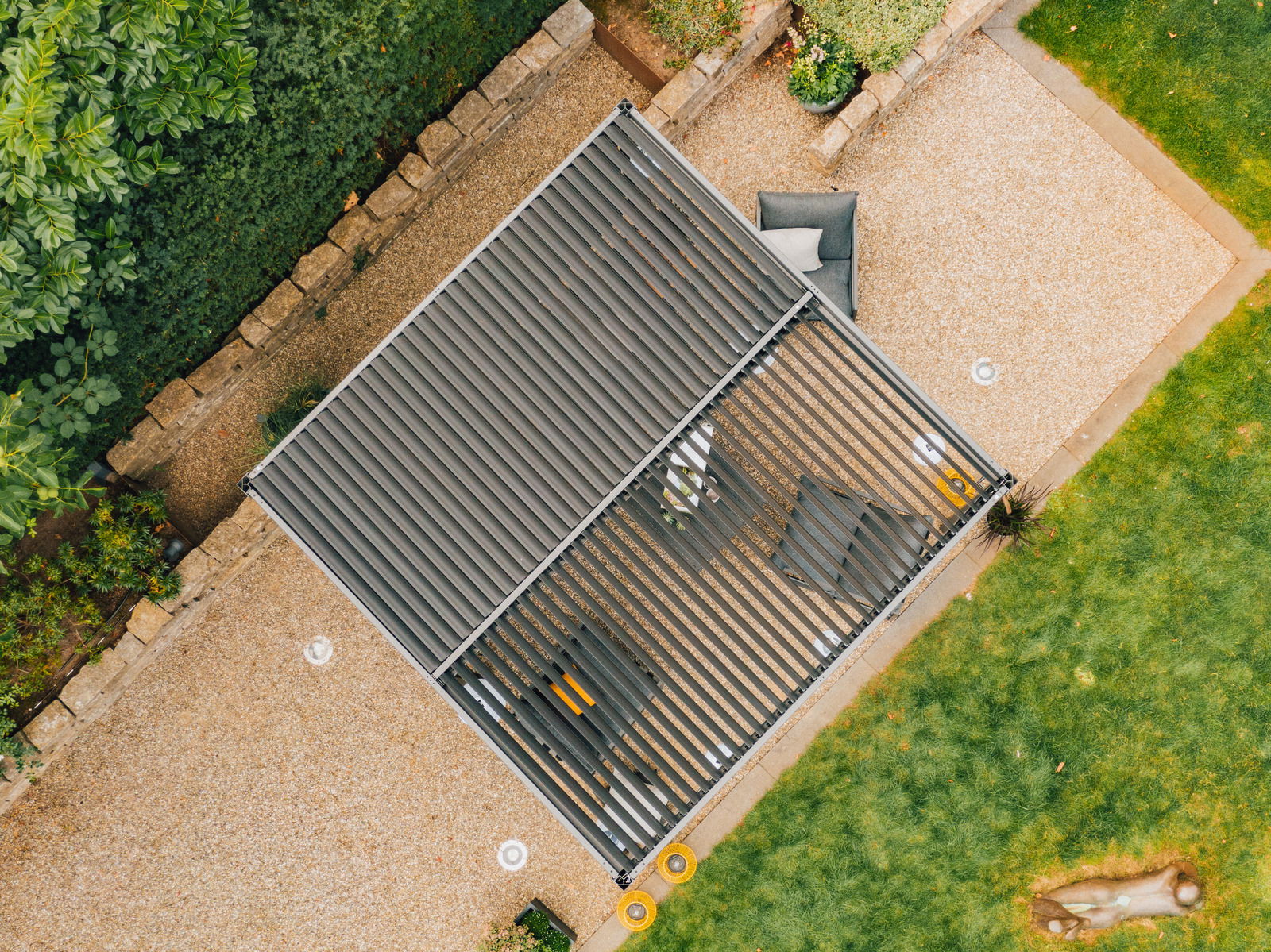Draufsicht auf eine moderne Terrassenüberdachung mit Lamellen, umgeben von einem gepflegten Garten und Sitzmöbeln.