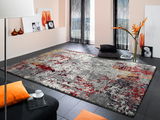 Designer Teppich mit abstraktem Muster in Grau, Rot und Gelb, in einem modernen Wohnzimmer mit schwarzem Boden und orangen Akzenten, aus der Perspektive von schräg oben fotografiert.