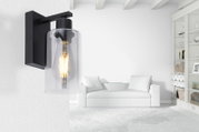 Moderne Wandleuchte mit schwarzem Metallrahmen und klarem Glaszylinder, seitliche Perspektive im Wohnzimmer.